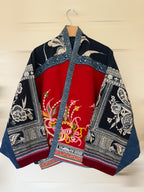 Traditional jacket with red and blue patterns on a wooden hanger against a beige wall.